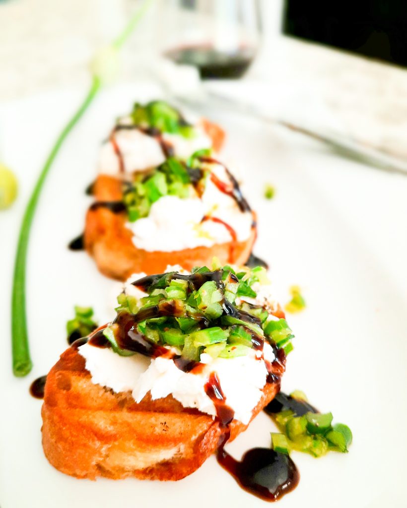 Leek scapes and goat cheese top a buttered grilled baguette slice