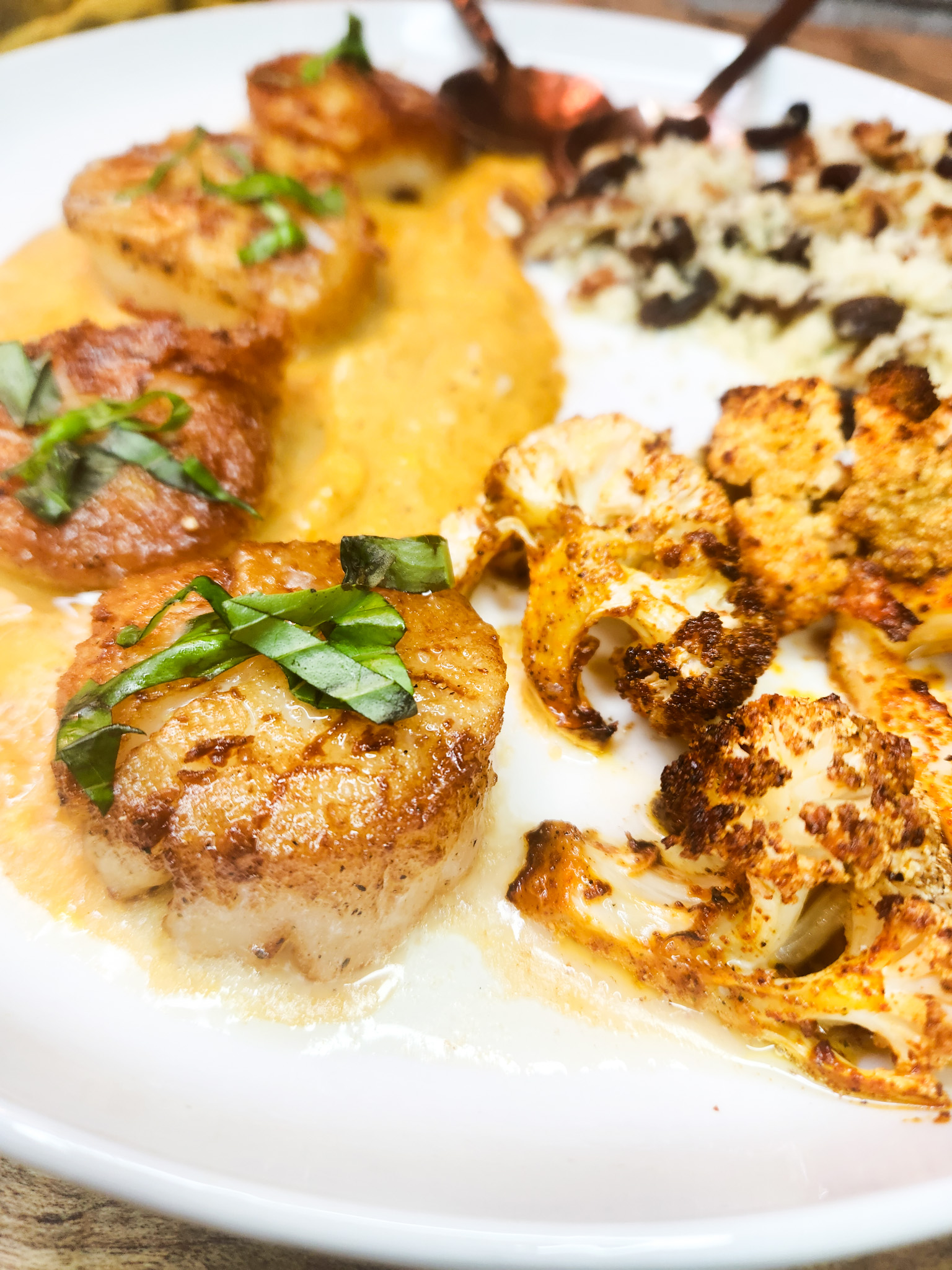 Indian Spiced Sea Scallops features garam masala infused butternut squash puree, roasted cauliflower and couscous with pecans and raisins.
