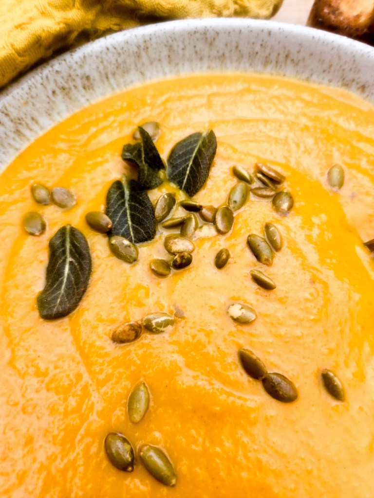 Acorn Squash Soup is warm and creamy with earthy spices like paprika, turmeric, cumin and chipotle, topped with fried sage and pepitas.