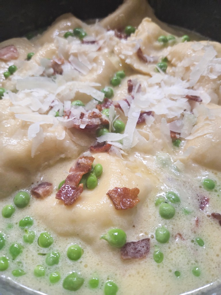 A close-up view of a creamy dish featuring dumplings, green peas, and bacon bits, topped with shredded cheese.