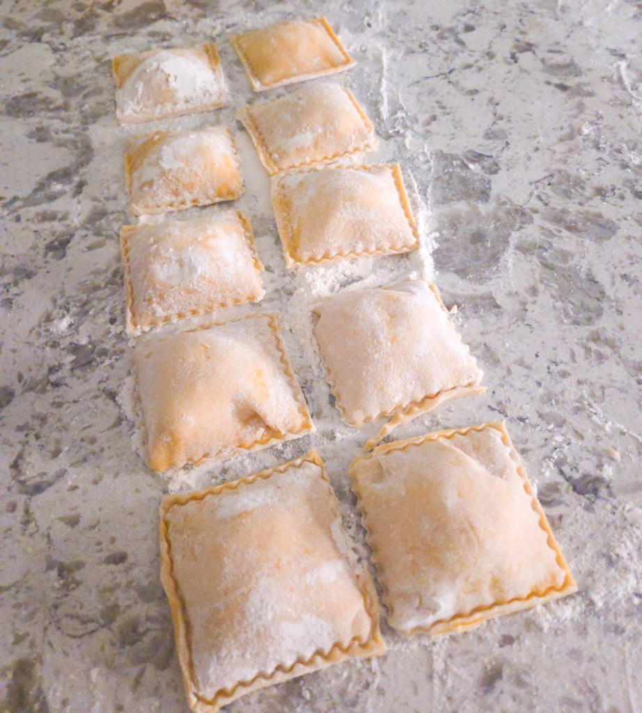 Freshly made ravioli dusted with flour, arranged in a row on a marble countertop.