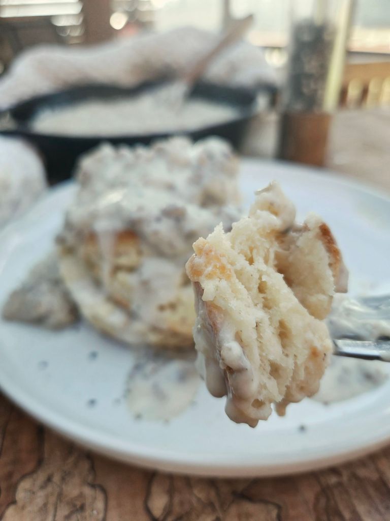 Close up bite of layered fluffy biscuit with creamy gravy