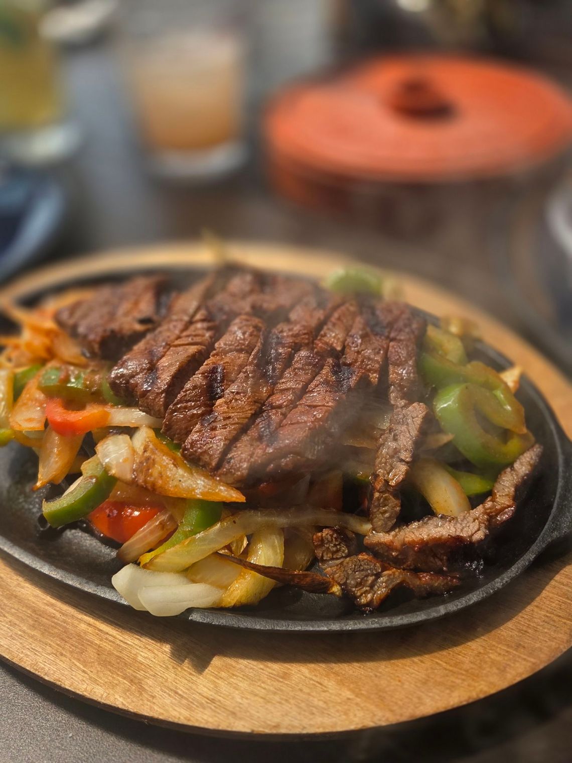 A sizzling plate of sliced steak and peppers and onions