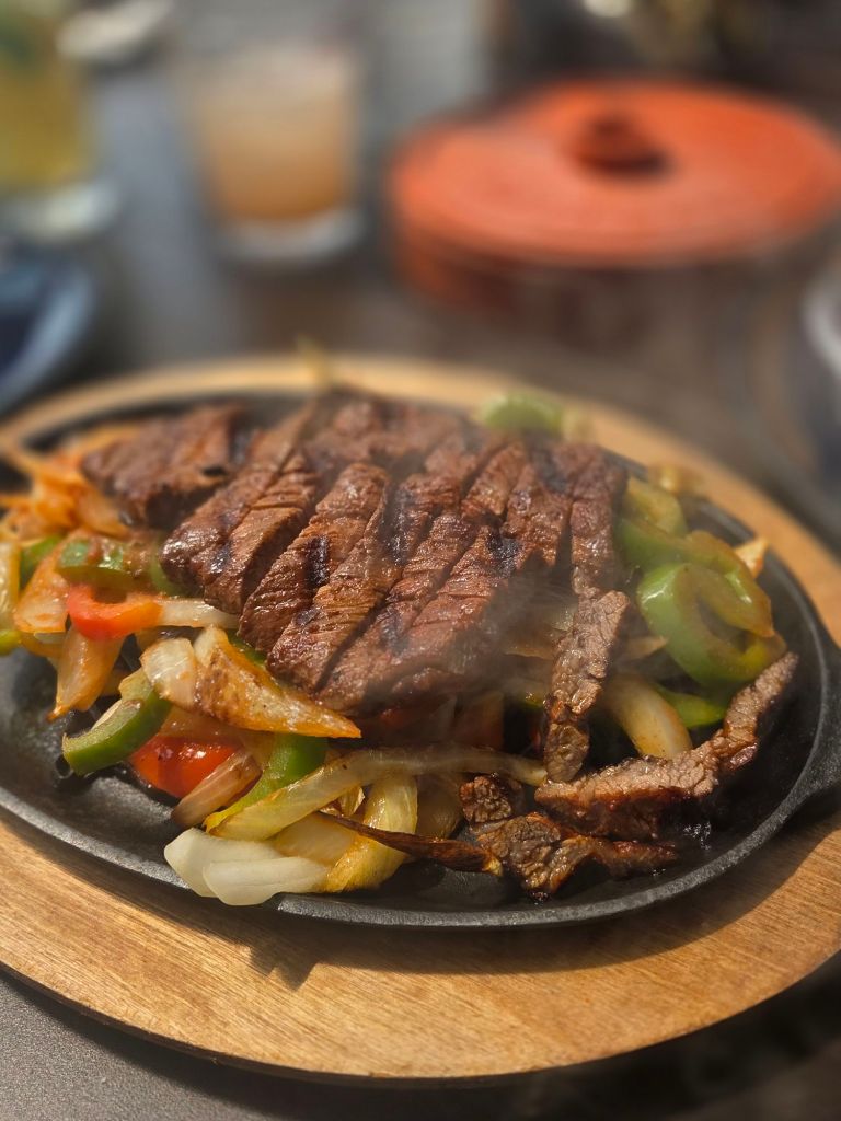 A sizzling plate of sliced steak and peppers and onions