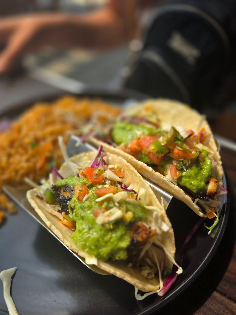Two tacos filled with grilled cod and topped with a green sauce with tomatoes and cabbage