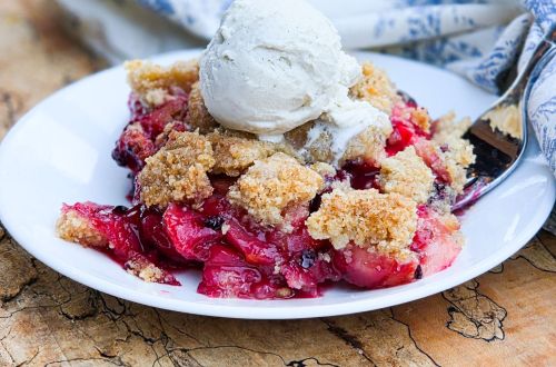 A slice of Blackberry Apple Crumble Pie topped with vanilla ice cream on a plate with a silver fork