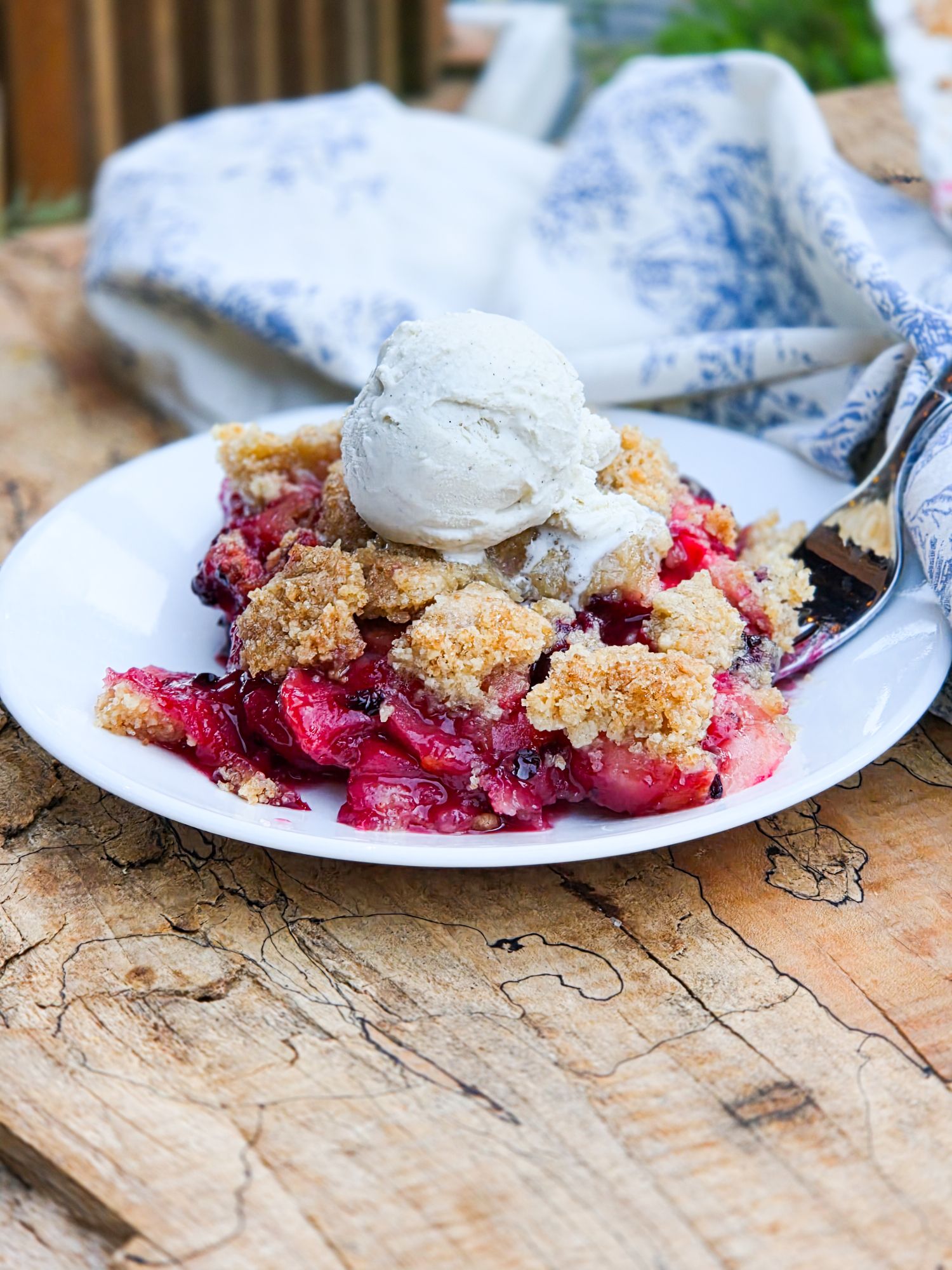A slice of Blackberry Apple Crumble Pie topped with vanilla ice cream on a plate with a silver fork