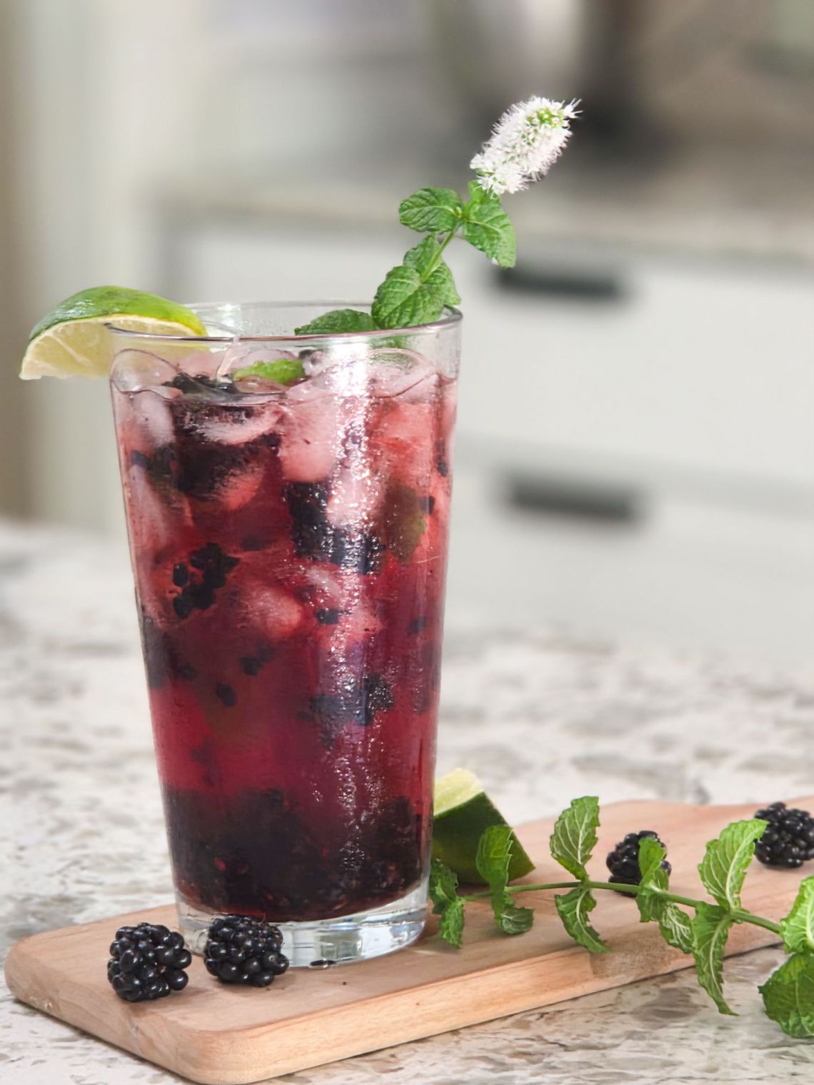 An ice filled glass of blackberry lime mojito with lime garnish and mint spring
