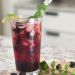 An ice filled glass of blackberry lime mojito with lime garnish and mint spring