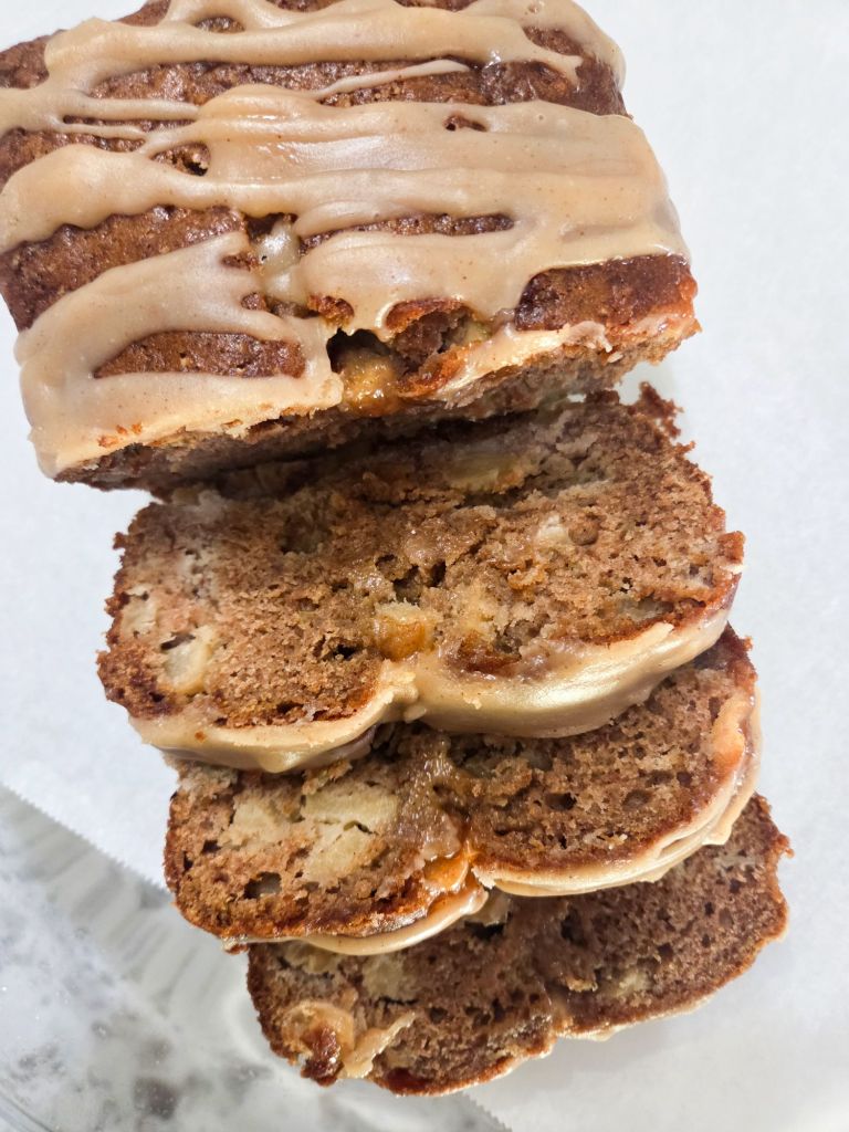 A loaf of apple cider bread with apple cider glaze drizzled over top and a couple sliced pieces