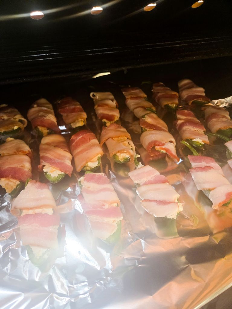 A sheet pan of many stuffed jalapeno poppers wrapped in bacon sitting on the smoker shelf