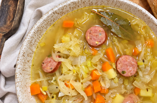 Overhead view of Polish sauerkraut soup with sausage, potatoes, and carrots, served with bread and sour cream.